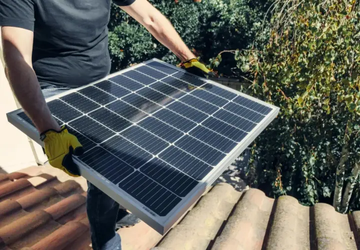 Person med gula handskar håller solpanel på taket. Undrar du vad kostar batteri till solceller?