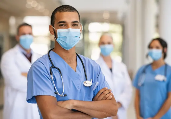 Un medico dello sport sorride, con colleghi sullo sfondo. Lo stipendio di un medico dello sport è una ricompensa per la dedizione.