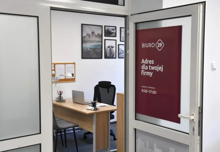 Widok biura rachunkowego z biurkiem, laptopem i tablicą ogłoszeń. Na drzwiach widnieje logo i godziny otwarcia.