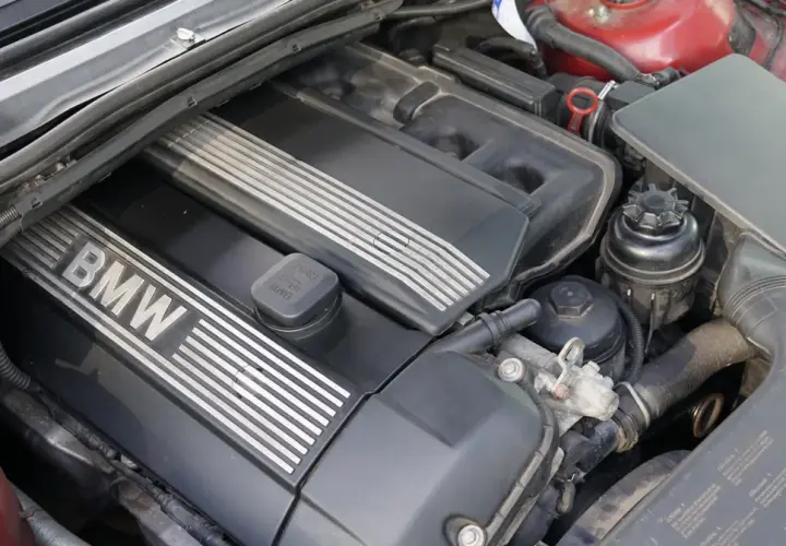 Silnik BMW e46, widok z góry. Czarna pokrywa silnika z napisem BMW i metalowymi wstawkami. Widać też elementy układu dolotowego i zbiorniczek płynu.