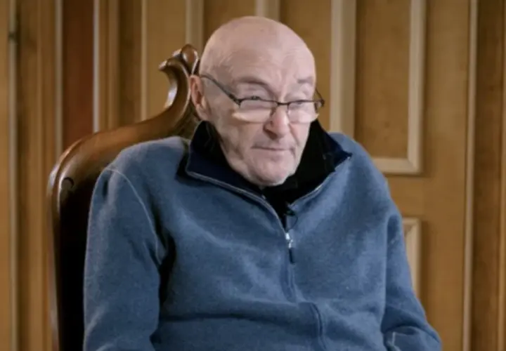 Phil Collins, zmagający się z chorobą, siedzi w fotelu, ubrany w niebieski polar.