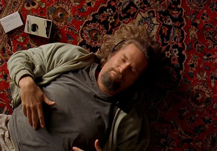 Un uomo con cuffie dorme su un tappeto persiano, accanto a un Walkman. Un'immagine iconica che evoca le recensioni de "Il Grande Lebowski".