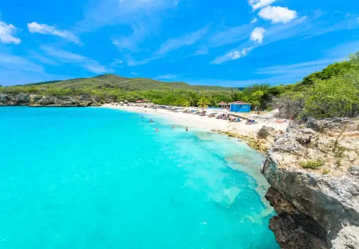Traumhafter Curacao Beach mit türkisblauem Wasser, weißem Sand, Liegestühlen und Menschen, die schwimmen und sich sonnen.