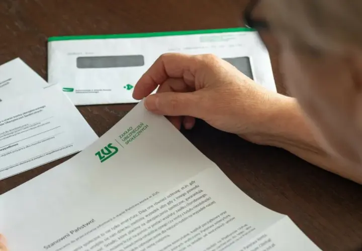 Dłoń przegląda dokumenty ZUS dotyczące zasiłku chorobowego i innych świadczeń.