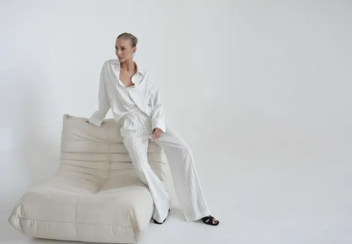 Elegancka kobieta w pasiastym komplecie, uosobienie quiet luxury, siedzi na kremowej sofie.