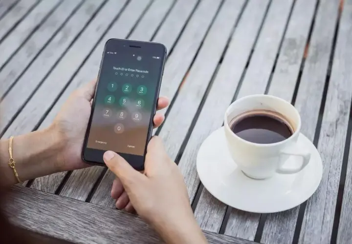Dłoń próbuje odblokować zablokowany iPhone, obok stoi filiżanka kawy.