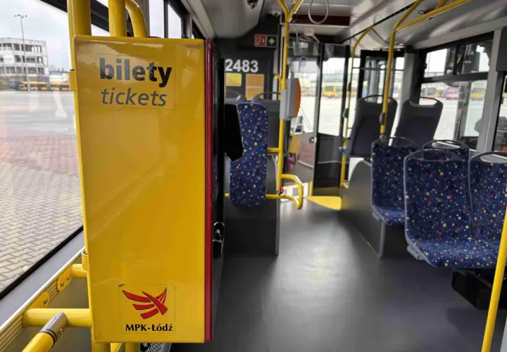 Wnętrze autobusu MPK-Łódź. Żółta skrzynka z napisem "bilety tickets" i logo MPK-Łódź. Widoczne siedzenia i poręcze.