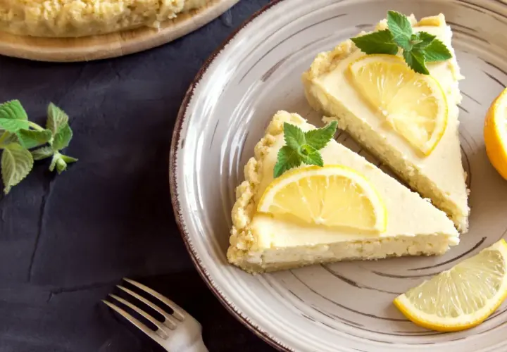 Dos porciones de tarta de limón, decoradas con rodajas de limón y hojas de menta, listas para ser disfrutadas.