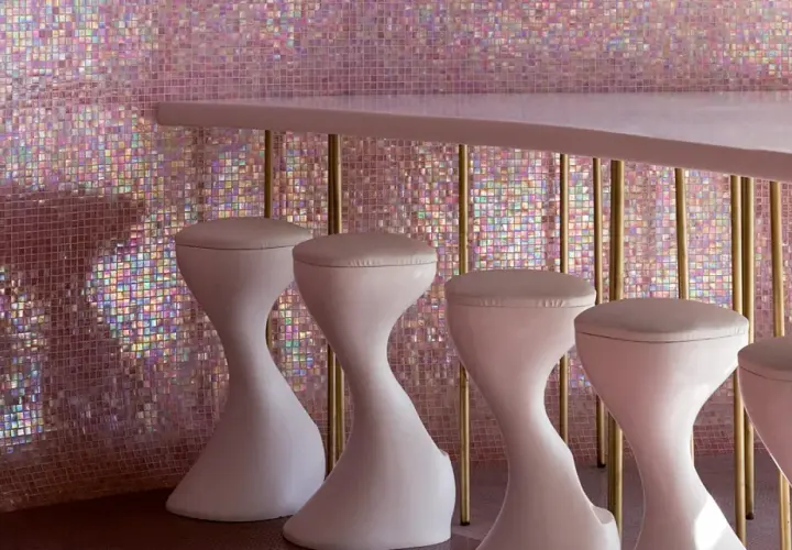 Un bancone rosa pallido con sgabelli bianchi si staglia contro un muro scintillante di **bisazza ceramiche** iridescenti, creando un'atmosfera glamour.
