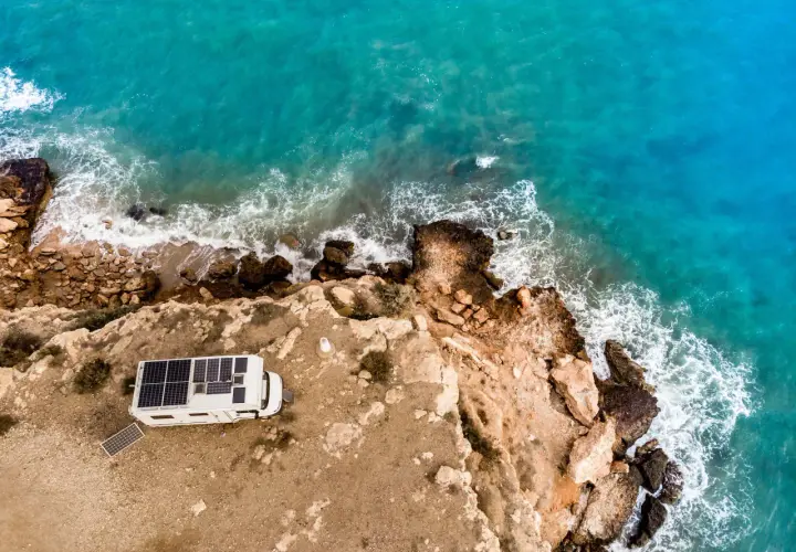Camping-car avec panneaux solaires sur une falaise en Espagne, face à la mer turquoise. Une belle escapade de camping chez l'habitant.