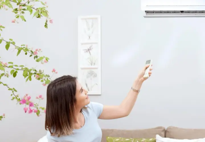 Mujer ajusta el aire acondicionado con control remoto. El vane del aire acondicionado significa confort y frescura en casa.