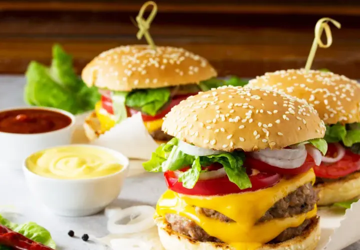 Tre succulenti burger roll con formaggio fuso, pomodoro, cipolla e lattuga, accompagnati da salse.