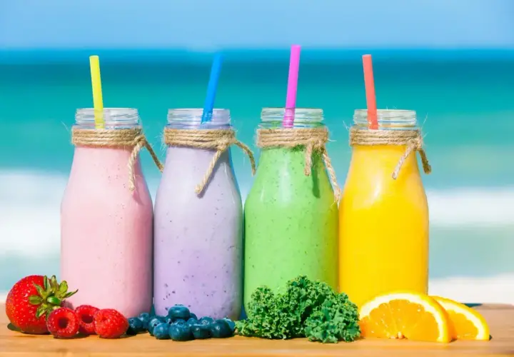 Cztery kolorowe smoothie na plaży: różowe, fioletowe, zielone i żółte. Idealne na lato, pokazują, jak zrobić smoothie z owoców i warzyw.
