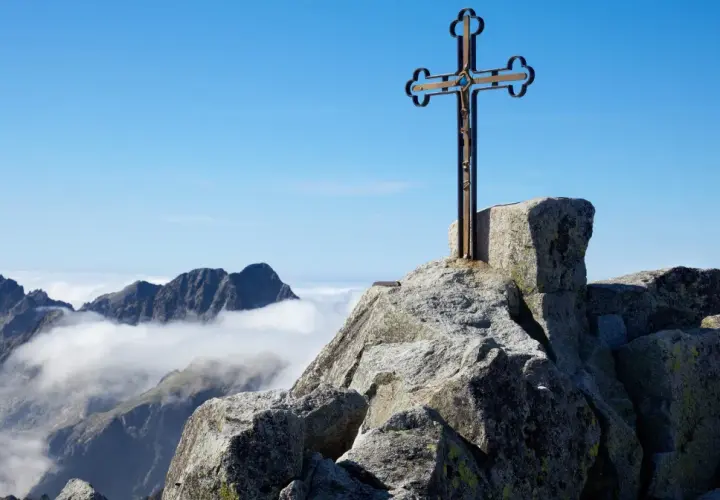 Krzyż na skalistym szczycie, najwyższy szczyt Tatr, góruje nad morzem chmur.