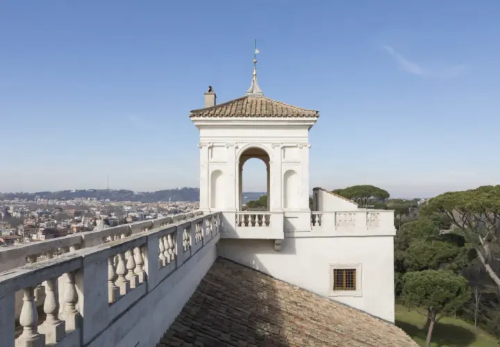 Vue panoramique de Rome depuis la Villa Médicis. Un belvédère blanc orné d'une arche domine le paysage urbain.