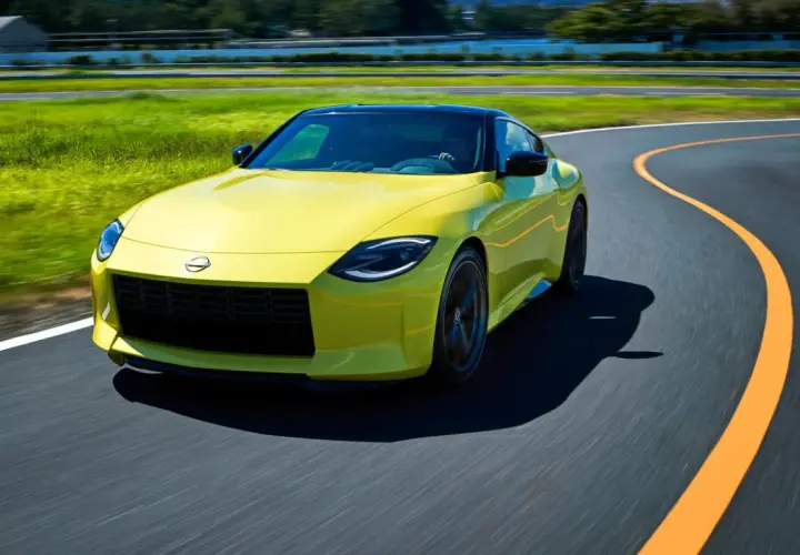 Gul Nissan 400Z kör på en kurvig bana med grönskande fält och träd i bakgrunden.