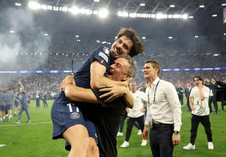 Radość piłkarza PSG obejmującego trenera. W tle tłum kibiców i stadion.