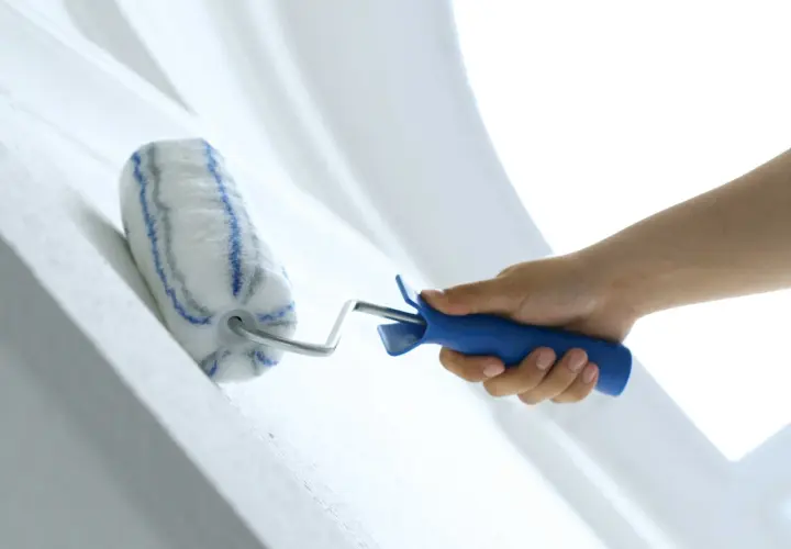 Hand streicht mit einer Farbrolle über eine weiße Wand. Der Putz wird frisch gestrichen.