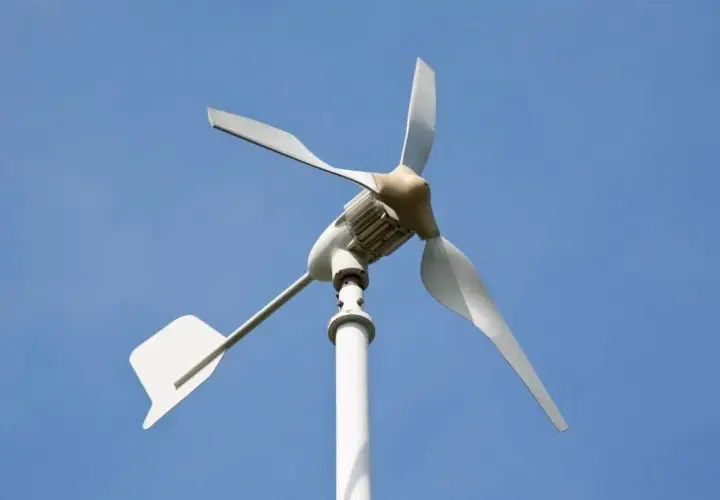 Biała elektrownia wiatrowa z trzema łopatami na tle błękitnego nieba.
