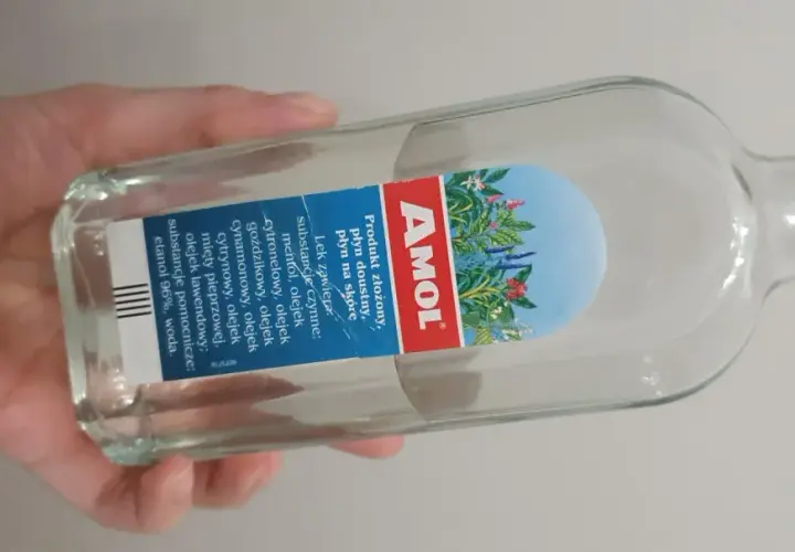 Dłoń trzyma butelkę Amolu. Ten lek, znany z dobrej ceny, zawiera mieszankę olejków eterycznych.