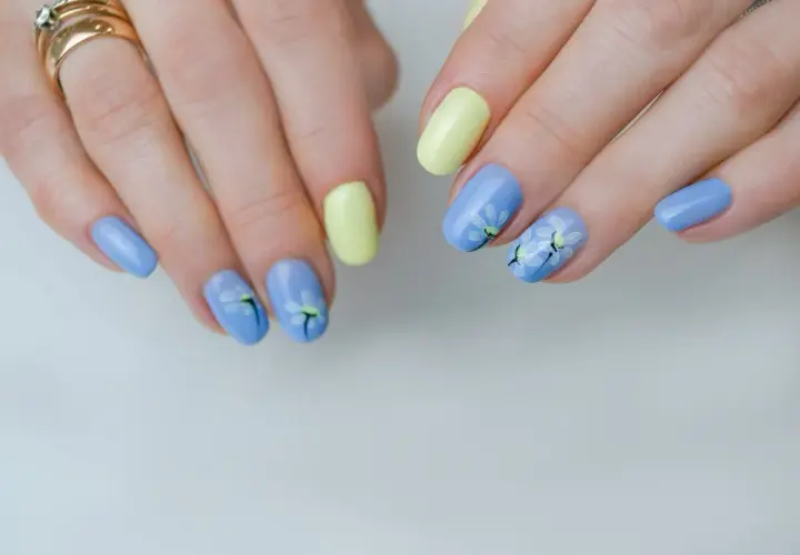 Delikatne kwiaty na paznokciach w pastelowych kolorach: błękitnym i żółtym. Wiosenny manicure z motywem stokrotek.