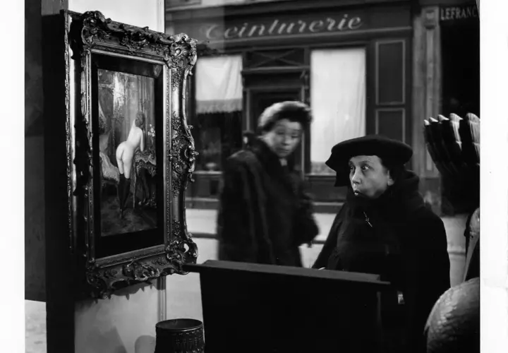 Una donna guarda un quadro in una vetrina, un'altra figura sfocata sullo sfondo. Robert Doisneau foto.
