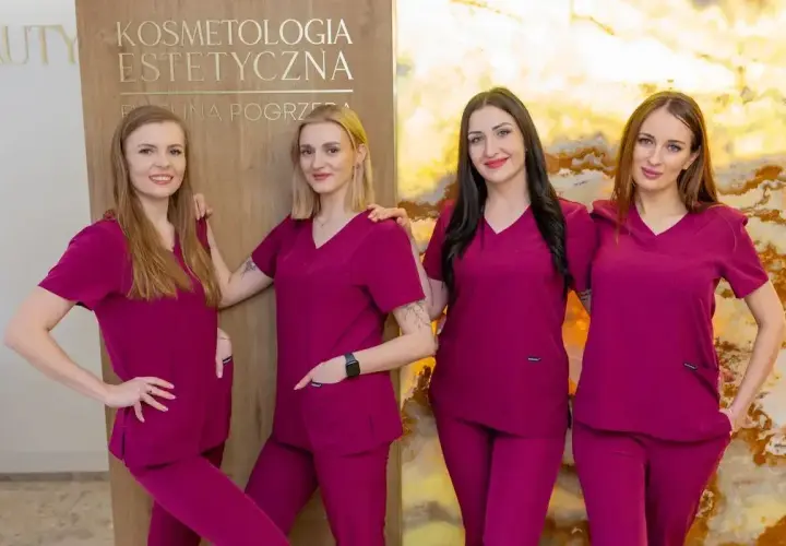 Cztery kobiety w uniformach medycznych stoją obok siebie przed tablicą z napisem "Kosmetologia Estetyczna".