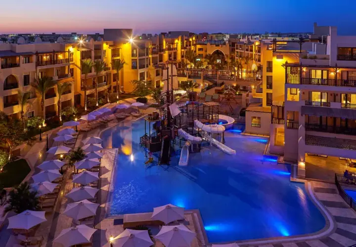 Wieczorem w Steigenberger Aqua Magic, basen z atrakcjami wodnymi i zjeżdżalniami, otoczony hotelowymi budynkami i leżakami pod parasolami.