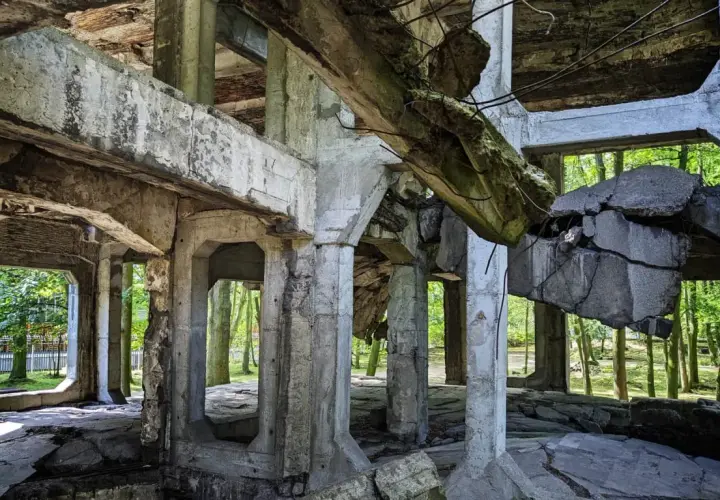 Ruiny koszar na Westerplatte podczas zwiedzania. Zniszczone betonowe konstrukcje i widok na drzewa.
