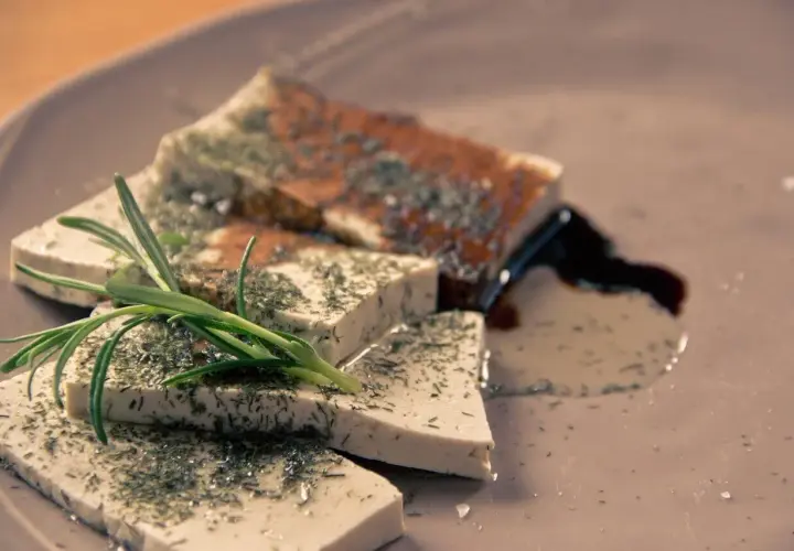 Queso tofu marinado con hierbas y romero, servido en un plato con salsa oscura.