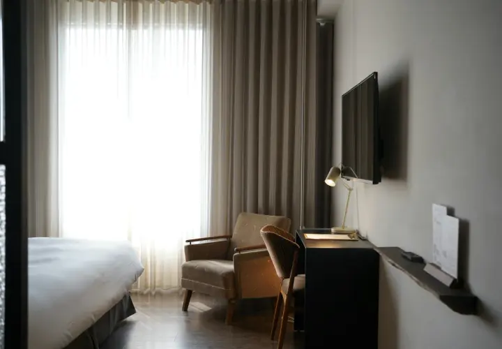 Przytulny pokój hotelowy z wygodnym łóżkiem, fotelem i biurkiem. Zastanawiasz się, ile kosztuje nocleg w takim miejscu?