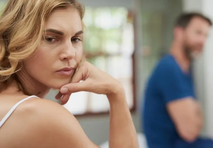 A woman looks worried, with a man blurred in the background.