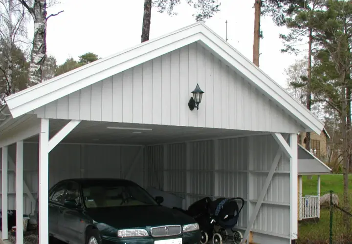 Vit carport på plintar med en bil och barnvagn.