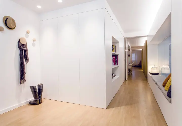 Un recibidor panelado moderno con suelo de madera, estanterías empotradas, un sombrero y bufanda colgados, y botas de montar.