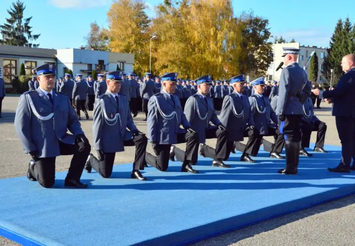 Uroczystość policyjna, policjanci w mundurach klęczą na niebieskim dywanie.