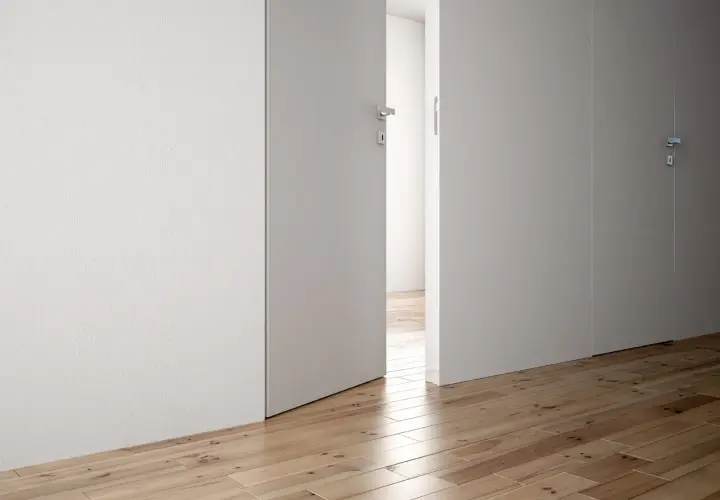 Parete di cartongesso con porta a battente aperta, che rivela un corridoio con parquet.