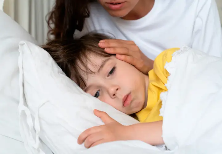 Madre reconforta a su hijo enfermo en la cama. Consejos sobre como calmar la tos en niños.