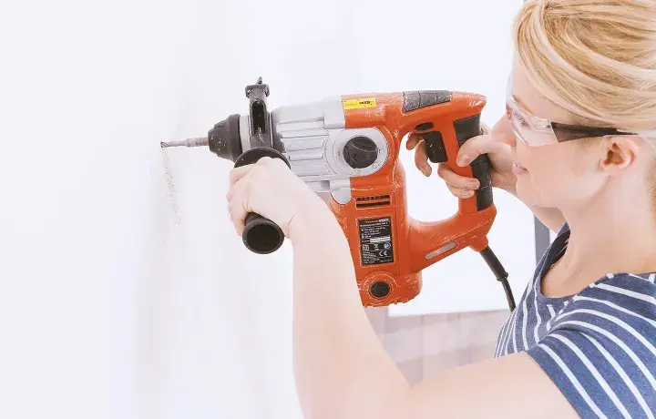 Femme avec lunettes de protection utilisant un marteau-perforateur pour percer du béton.
