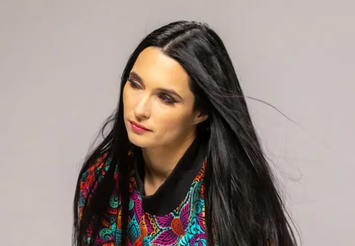 Portret kobiety z długimi, czarnymi włosami w kolorowej bluzce. Emilia Sanecka, data urodzenia.