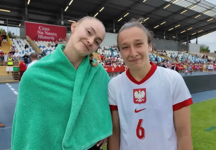 Dwie młode piłkarki w strojach reprezentacji Polski na tle trybun stadionu.