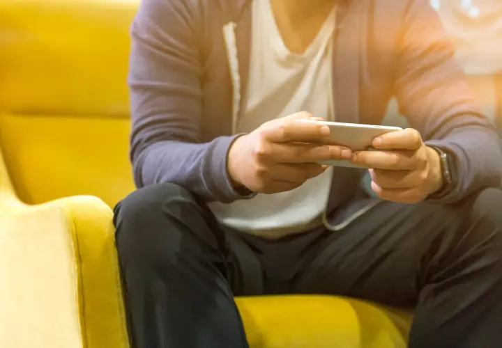 Mężczyzna siedzi na żółtym fotelu, grając na telefonie. Nawet poza siecią, jego **tuya smart** urządzenia działają bez zarzutu.