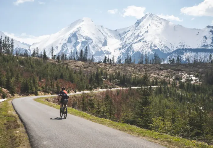 Rowerzysta na krętej drodze z widokiem na ośnieżone Tatry. Marzenie o rowerem dookoła Tatr w jeden dzień staje się rzeczywistością.