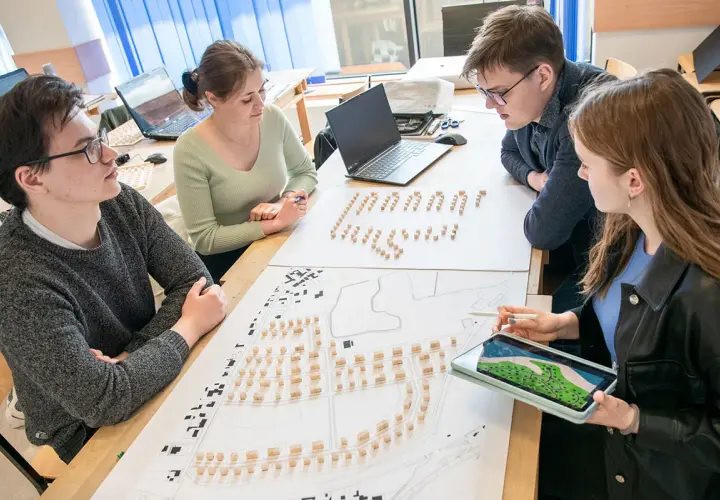 Studenci architektury analizują projekt urbanistyczny z makietą i planami.