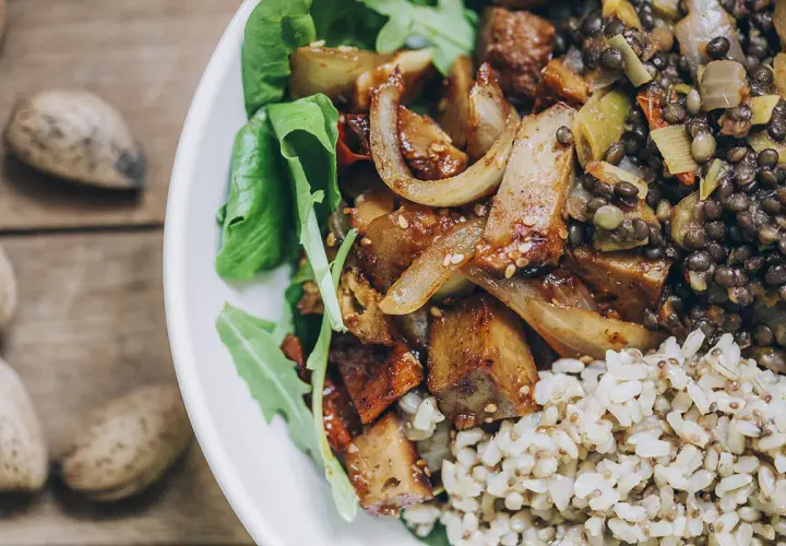 Plato con seitan salteado, lentejas, arroz integral y hojas verdes. Una deliciosa opción para tus recetas de seitan.