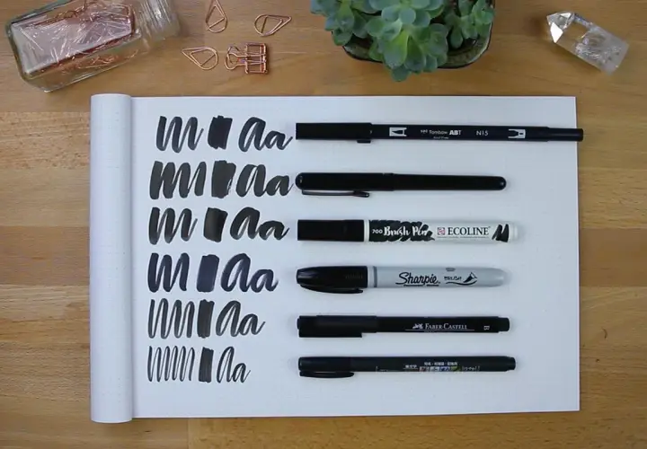 Práctica de lettering con varios rotuladores, mostrando trazos y letras "m" y "a" en un cuaderno.