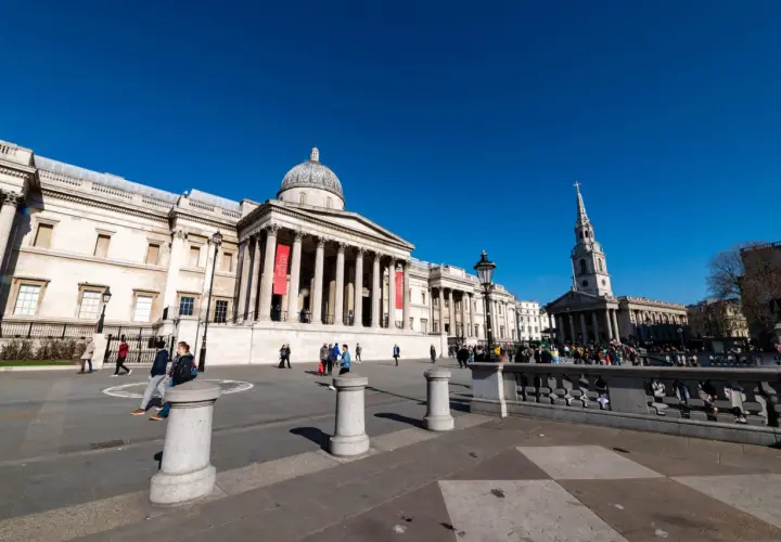 Trafalgar Square w Londynie, z National Gallery w tle. Wiele osób spaceruje po placu, ciesząc się darmowymi muzeami Londyn.