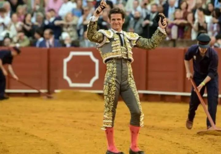 El Juli, torero con traje de luces, levanta las manos en la arena.