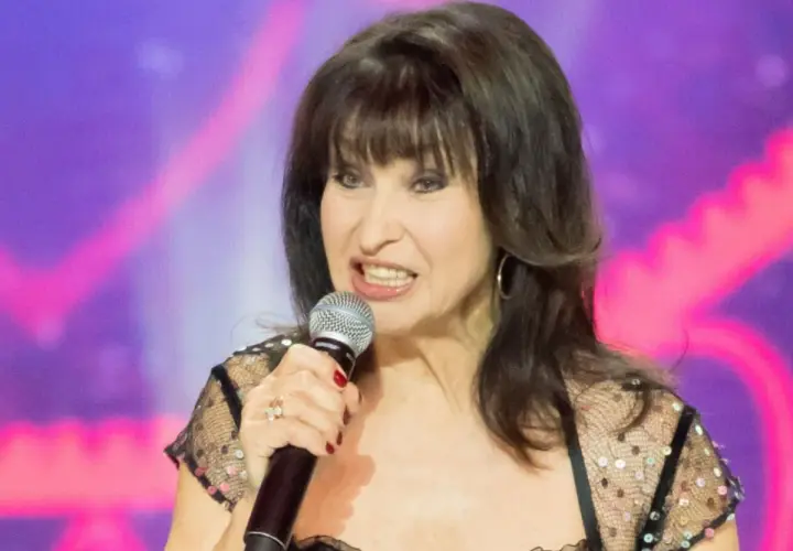 Krystyna Giżowska śpiewa do mikrofonu, w czarnej, błyszczącej sukience. Wiele osób zastanawia się, ile lat ma Krystyna Giżowska.