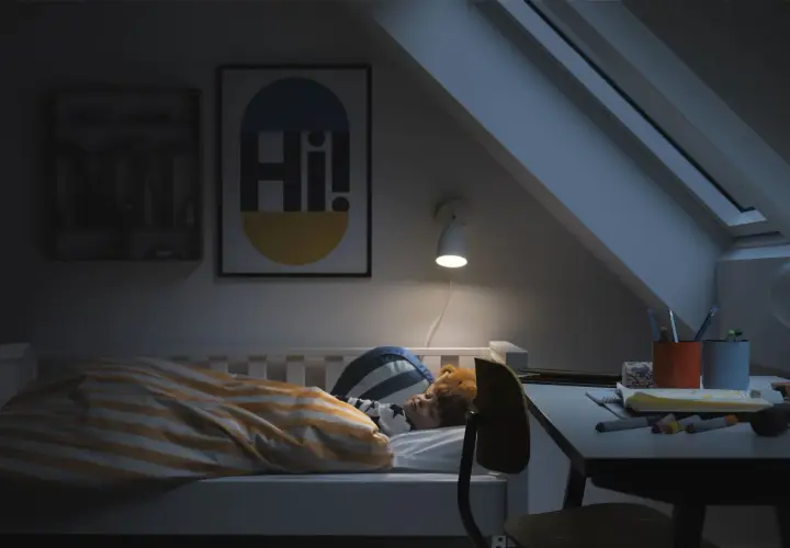 Barn sover i säng med randigt täcke. En lampa lyser över skrivbordet. God ventilation sovrum krav är viktigt för en god natts sömn.