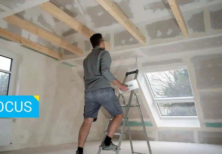 Un operaio su una scala lavora al soffitto, applicando stucco su pannelli di fibrogesso, materiale versatile per ristrutturazioni.